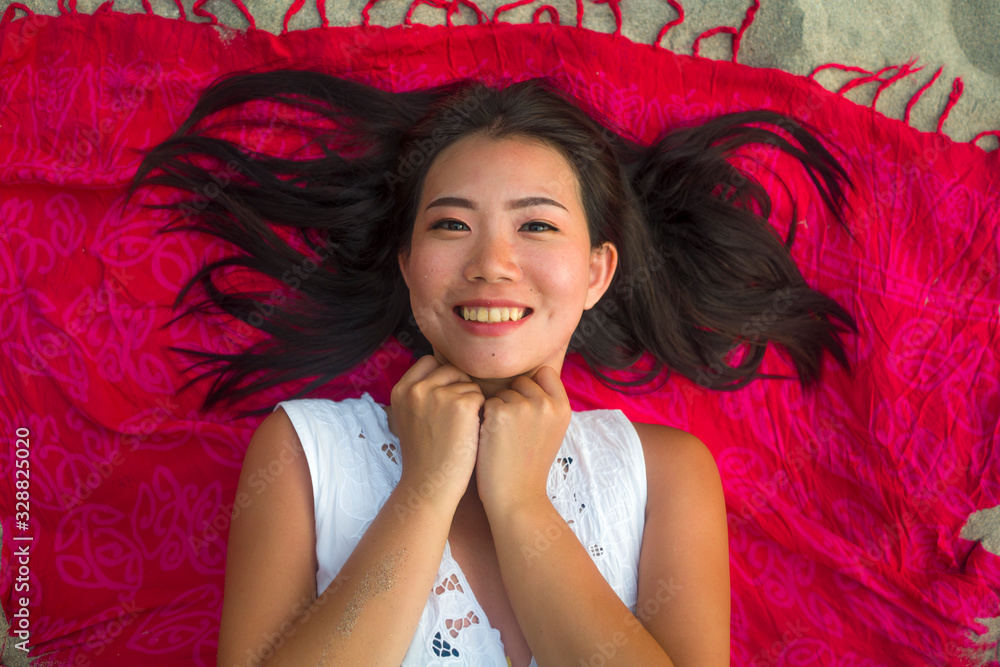 outdoors fresh and natural portrait of young beautiful and happy Asian Cchinese woman lying flat on sarong on beach sand smiling cheerful and relaxed