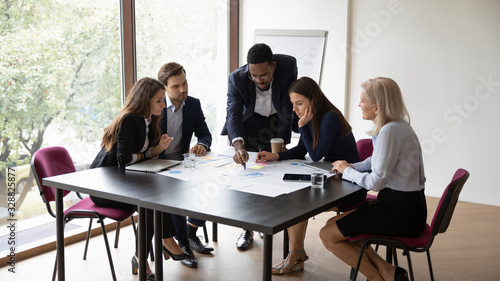 Diverse multiracial businesspeople gather in office brainstorm discuss company financial paperwork together, concentrated multiethnic colleagues cooperate in boardroom, consider project at briefing
