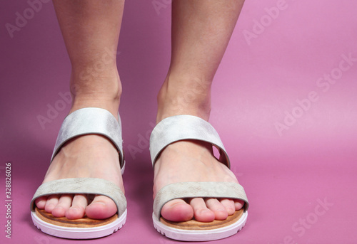 Female legs in trendy leather sandals on pink background. Summer footwear. Your stylish loook