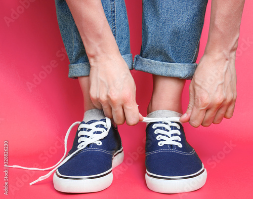 Woman tying shoelace of fashionable hipster sneakers over pink background