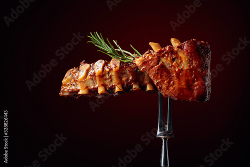 Grilled pork ribs with rosemary on a fork. Dark red background.