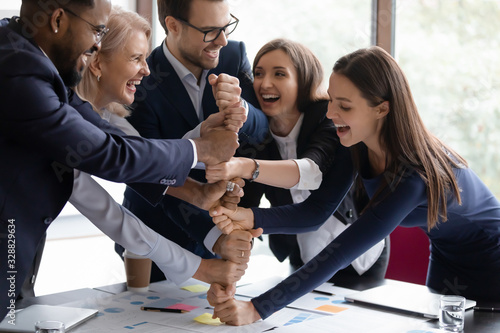 Overjoyed diverse businesspeople stack fist engaged in funny teambuilding activity at office meeting together, happy motivated multiracial employees join hands show unity and support, teamwork concept photo