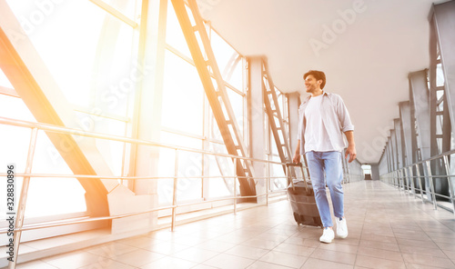 Happy man walking with suitcase in airport terminal © Prostock-studio