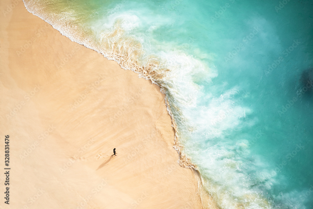 View from above, stunning aerial view of a person walking on a beautiful beach bathed by a turquoise sea during sunset. Kelingking beach, Nusa Penida, Indonesia.
