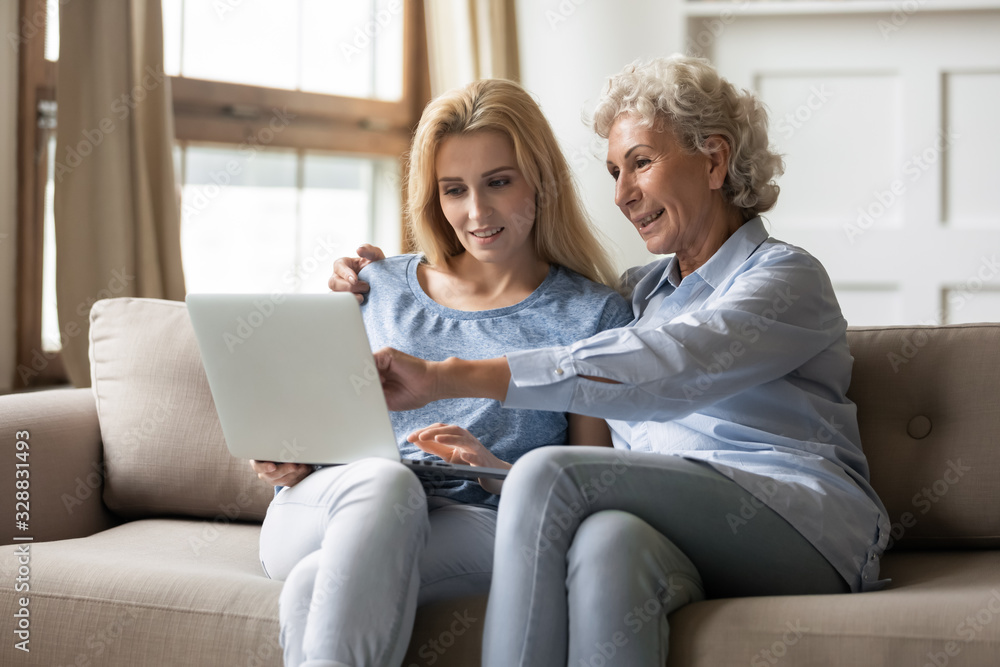 Senior mom and adult daughter sit on couch in living room browsing surfing wireless internet on laptop together, happy mature mother and millennial girl relax at home using modern computer gadget Senior mom and adult daughter sit on couch in living room browsing surfing wireless internet on laptop together, happy mature mother and millennial girl relax at home using modern computer gadget