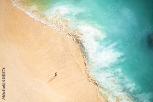 Obraz na płótnie View from above, stunning aerial view of a person walking on a beautiful beach bathed by a turquoise sea during sunset. Kelingking beach, Nusa Penida, Indonesia. w salonie