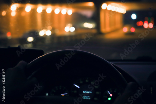Man hands driver on steering wheel of a modern car with Car dashboard and night city background. Traffic jam on rush hour in the city. Transport, Holiday, Travel and Automobile Concept.