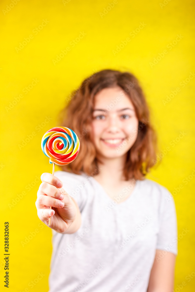 Teen girl holds out a multi-colored round lollipop in her hand