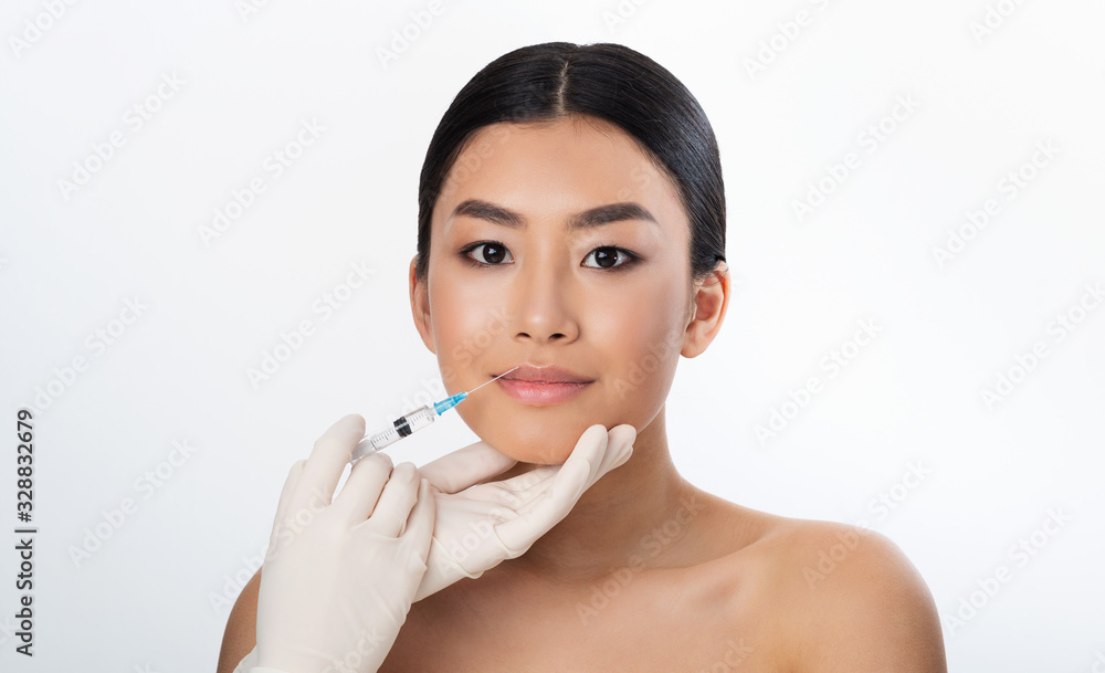 Korean Girl Receiving Injection During Lips Plumping Procedure, White Background Korean Girl Receiving Injection During Lips Plumping Procedure, White Background