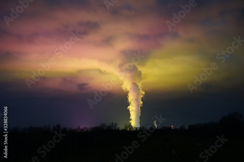 surreal light at night from the lit green houses on a cloudy sky with steam rising from the nuclear power plant