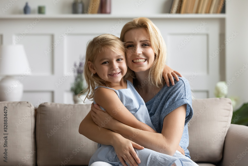 Portrait of smiling young mother and cute little preschooler daughter sit on couch in living room look at camera, happy mom and small girl child hug embrace relax on sofa at home, bonding concept Portrait of smiling young mother and cute little preschooler daughter sit on couch in living room look at camera, happy mom and small girl child hug embrace relax on sofa at home, bonding concept