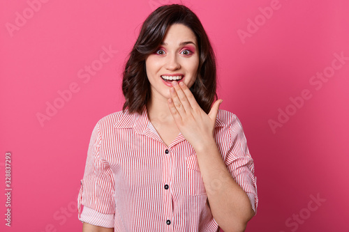 Indoor shot of surprised woman covering her mouth with hands while posing over pink background and looking at camera with opened mouth, female wearing casual outfit. People emotions concept.