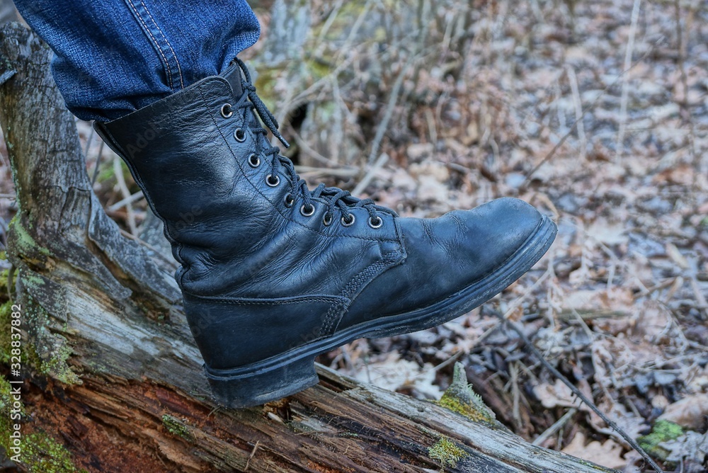 one black high army leather boot on a foot stands on a brown tree log in nature one black high army leather boot on a foot stands on a brown tree log in nature