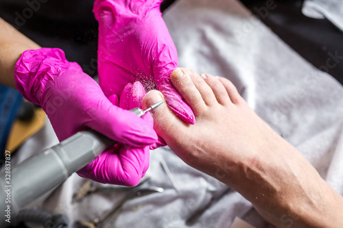 Valokuva Pedicurist master in pink gloves cuts the cuticle and shellac toe nails in the pedicure salon using drill