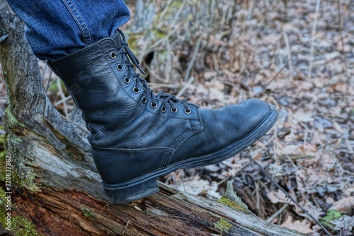 one black high army leather boot on a foot stands on a brown tree log in nature