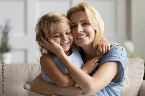 Portrait of happy young mother play hug and cuddle show love cute small preschooler daughter relaxing in living room, smiling mom and little girl child rest enjoy family weekend at home together