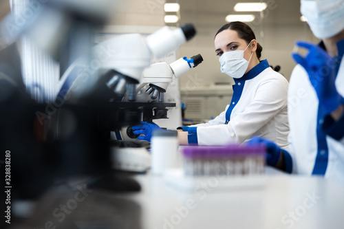 Female researcher in medical mask using microscope in lab