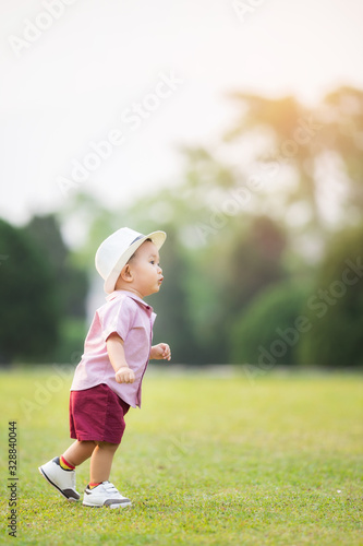 Asia baby boy wearing pink shirt and red pants with white hat walking in garden.