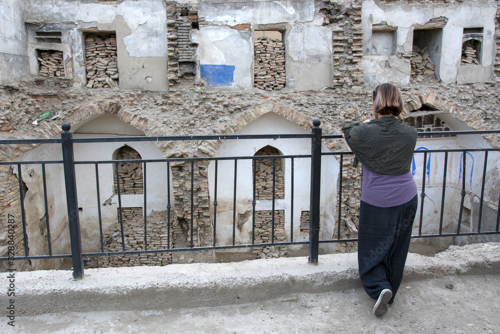 An European tourist (girl) looking at ruins of madrasah. Bukhara, Uzbekistan, Central Asia.