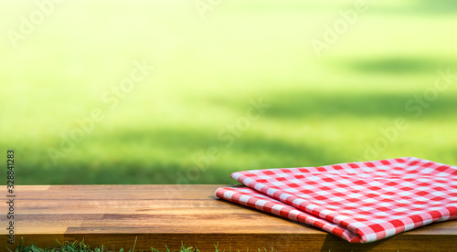 Red checked tablecloth on wood with blur green courtyard background.Summer and picnic concepts