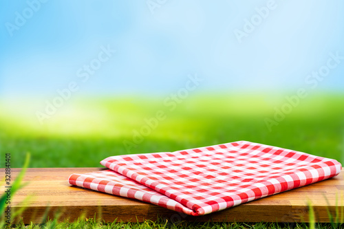 Red checked tablecloth on wood with blur green courtyard background.Summer and picnic concepts.Design for key visual food and drink products