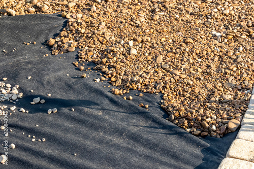 Spreading river pebble over the laid woven geotextile fabric in the summer garden under reconstruction