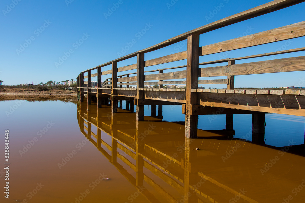 view of a wooden bridge at a lagoon or lake with brown waters, pedestrian bridge over lake, wooden bridge artificial lake, ancient salt flats in Roquetas de Mar, Almeria, Andalusia, Spain