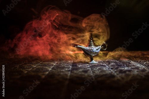 Lamp of wishes concept. Antique Aladdin arabian nights genie style oil lamp with soft light white smoke, Dark background.