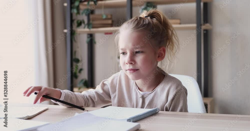 Funny elementary school child girl studies alone talks to herself feels bored, annoyed or tired. Cute lazy 6-7 years kid having difficulty with homework at home. Problem in children education concept Funny elementary school child girl studies alone talks to herself feels bored, annoyed or tired. Cute lazy 6-7 years kid having difficulty with homework at home. Problem in children education concept