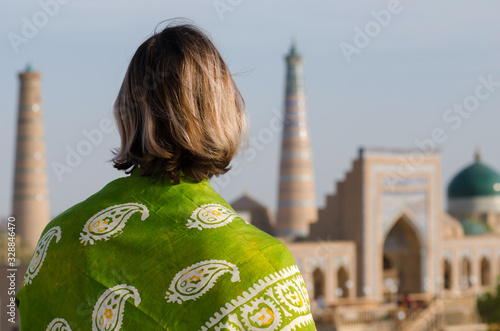 Young european woman with shawl on the background of old town (minaret, madrasah, mausoleum). Khiva, Uzbekistan, Central Asia.