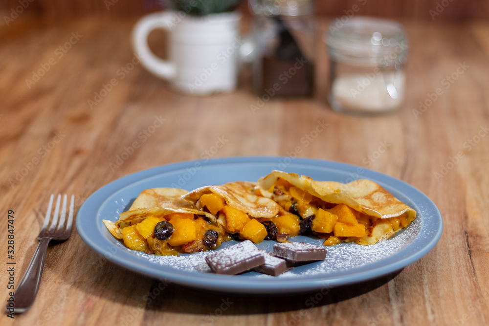 Mango crepes, with 3 chocolate feet, on a blue plate on a wooden table