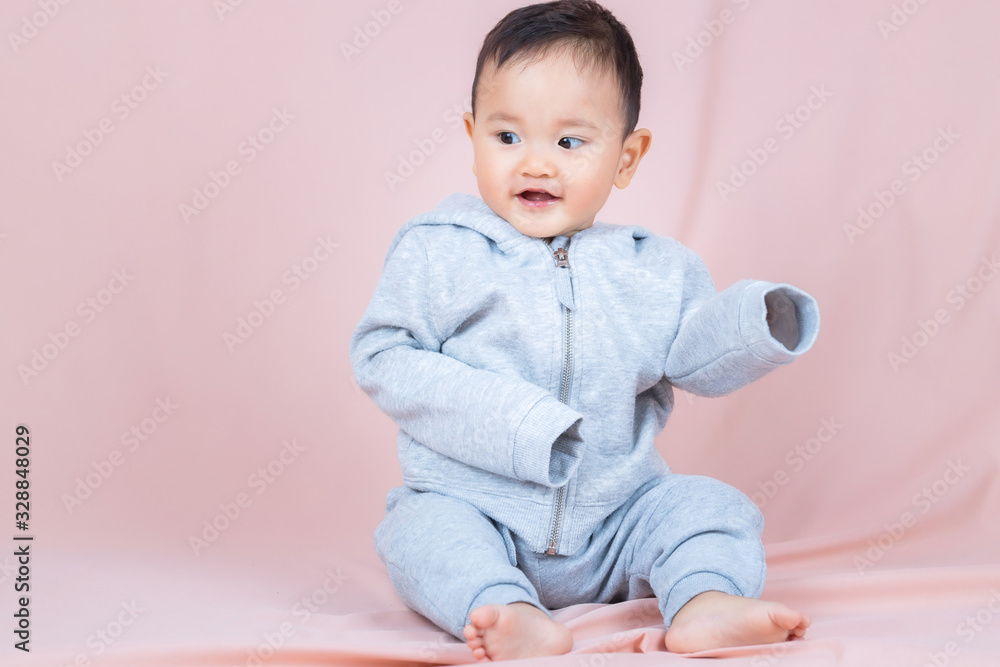 Asia baby boy wearing gray shirt and pants, sitting on floor and peach background. Asia baby boy wearing gray shirt and pants, sitting on floor and peach background.