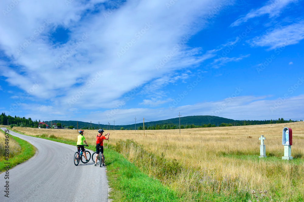 Cyclist taking pictures with smart phone. Man in bike helmet taking photo of roadside shrine. Outdoor activity in Low Beskids, Poland. Cyclist taking pictures with smart phone. Man in bike helmet taking photo of roadside shrine. Outdoor activity in Low Beskids, Poland.