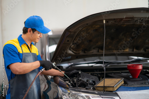 auto mechanic wearing protective work gloves holding a dirty, air filter over a car engine for cleaning