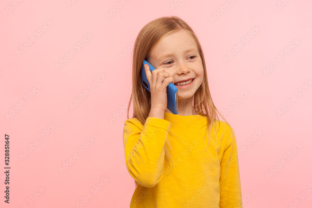 Cute little ginger girl with freckles smiling joyfully while calling parents on cell phone, good cellular, roaming, comfortable to use children mobile device. studio shot isolated on pink background Cute little ginger girl with freckles smiling joyfully while calling parents on cell phone, good cellular, roaming, comfortable to use children mobile device. studio shot isolated on pink background