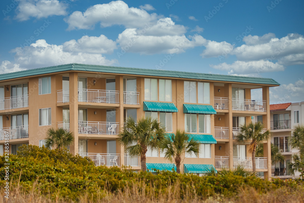 A coastal condo building of pink stucco with green metal roof and awnings