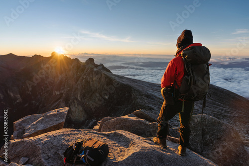 a man with backpack enjoying sunrise over the clouds on Kota Kinabalu summit in Malaysia. Travel lifestyle, adventure and outdoor activity photo