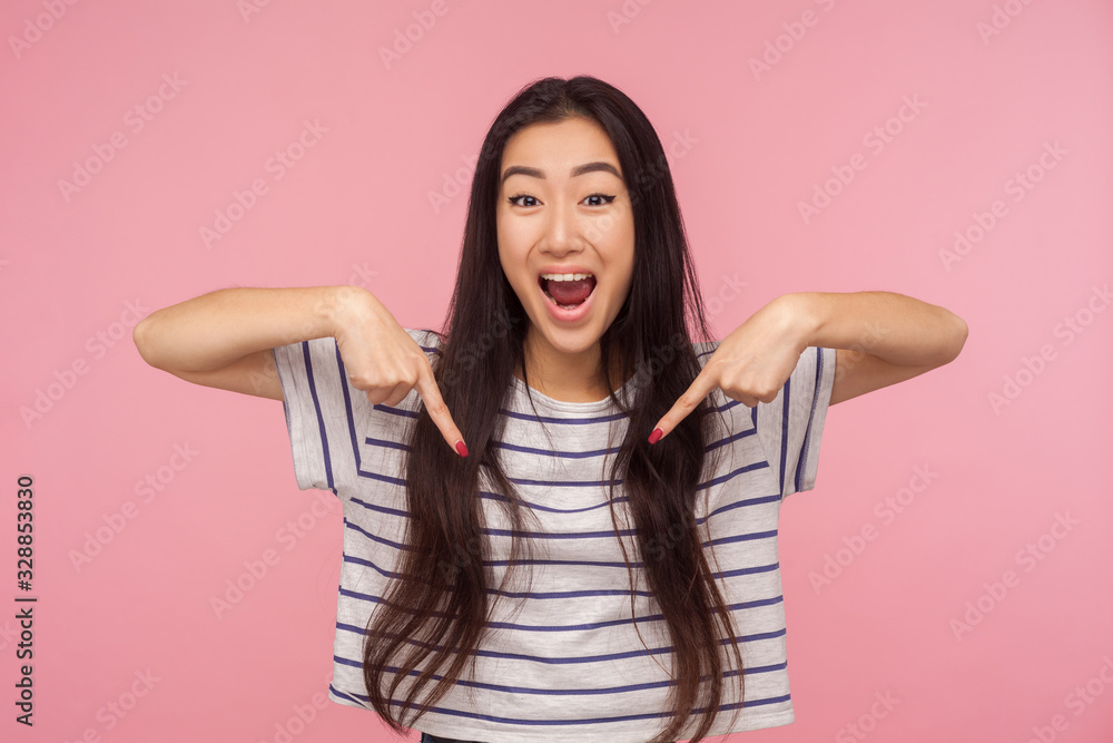 Wow look at advertise! Portrait of excited, surprised girl in striped t-shirt pointing down and looking with shocked face, showing place for commercial. indoor studio shoot isolated on pink background Wow look at advertise! Portrait of excited, surprised girl in striped t-shirt pointing down and looking with shocked face, showing place for commercial. indoor studio shoot isolated on pink background