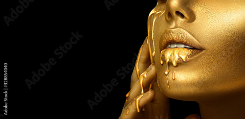 Gold Paint smudges drips from the face lips and hand, lipgloss dripping from sexy lips, golden liquid drops on beautiful model girl's mouth, gold metallic skin make-up. Beauty woman makeup close up. © Subbotina Anna