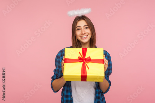 Present from angel. Portrait of generous happy beautiful girl with halo over head holding gift box and smiling kindly, congratulating on birthday. indoor studio shot isolated on pink background