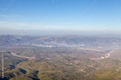 Areal view of a curvy highway road going through the valleys and forest with background mountains and blue sky