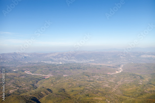 Areal view of a curvy highway road going through the valleys and forest with background mountains and blue sky © Nikola