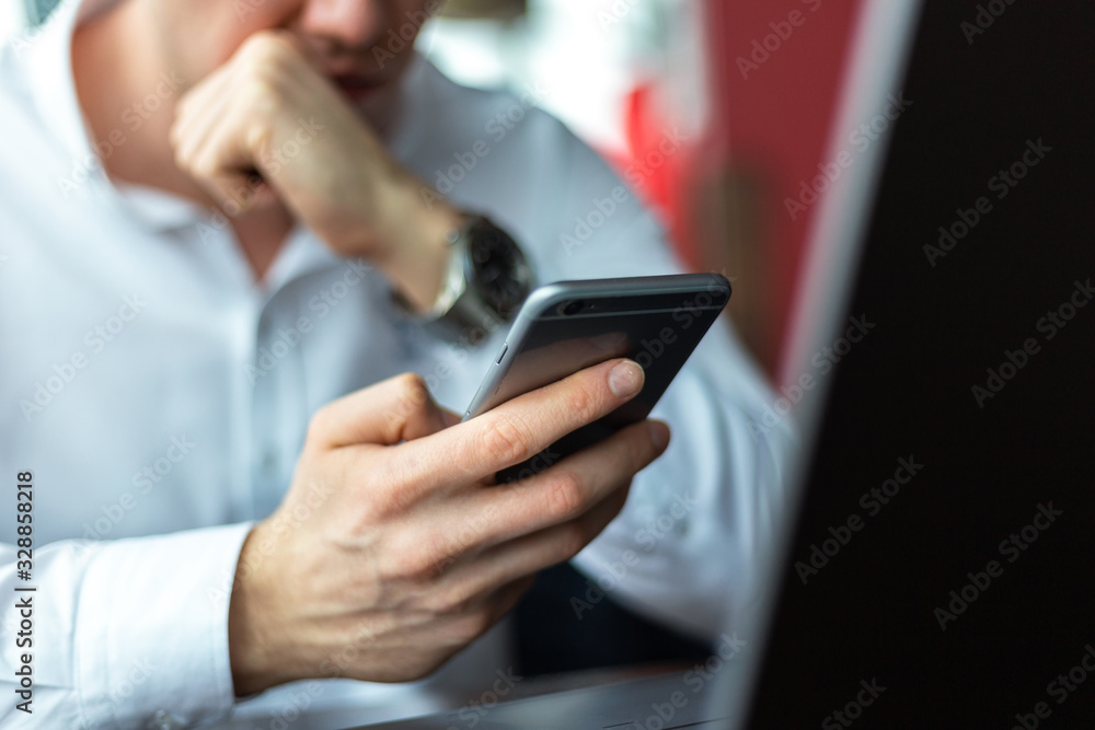 Closeup of hands of young businessman wearing a white fashion shirt with a mobile phone in a cafe with a laptop and documents. Freelance and selfemployment concept. Distance job.