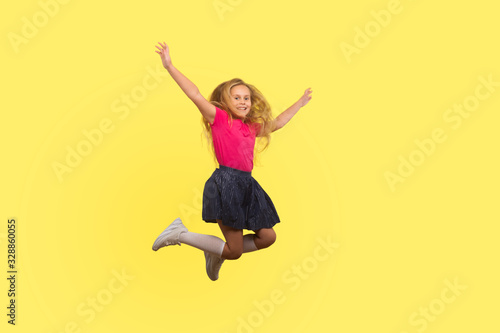Full length portrait of beautiful little girl with long blond hair in dress jumping in air, inspired child flying and celebrating carefree life. indoor studio shot isolated on yellow background