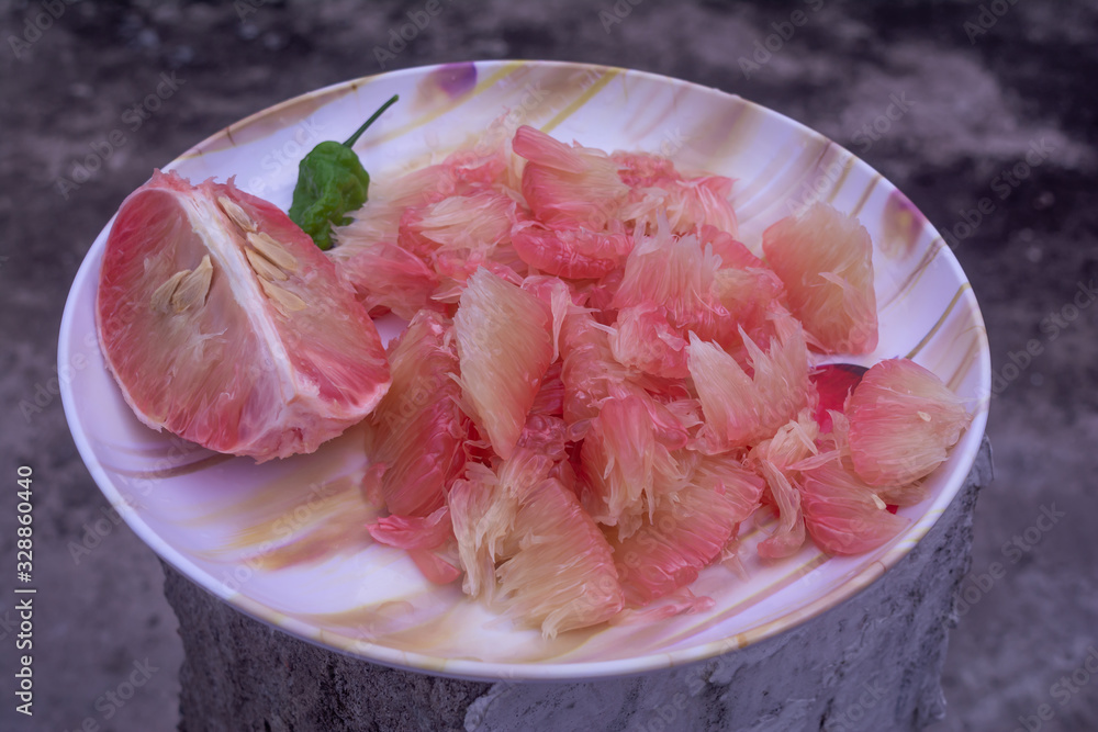 POMELO (ROBAB TENGA) CITRUS FRUIT INNER PARTS WITH GHOST CHILI PEPPER (BHUT JOLOKIA) IN A PLASTIC PLATE PLACED ON GREY SURFACE PILLAR