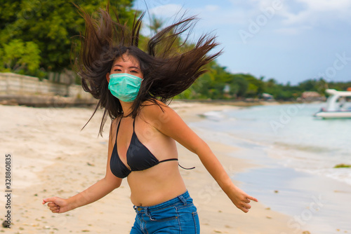 use of medical face mask in public places- young attractive Asian Chinese woman enjoying beach holidays wearing bikini and protective facial mask in prevention vs virus infection