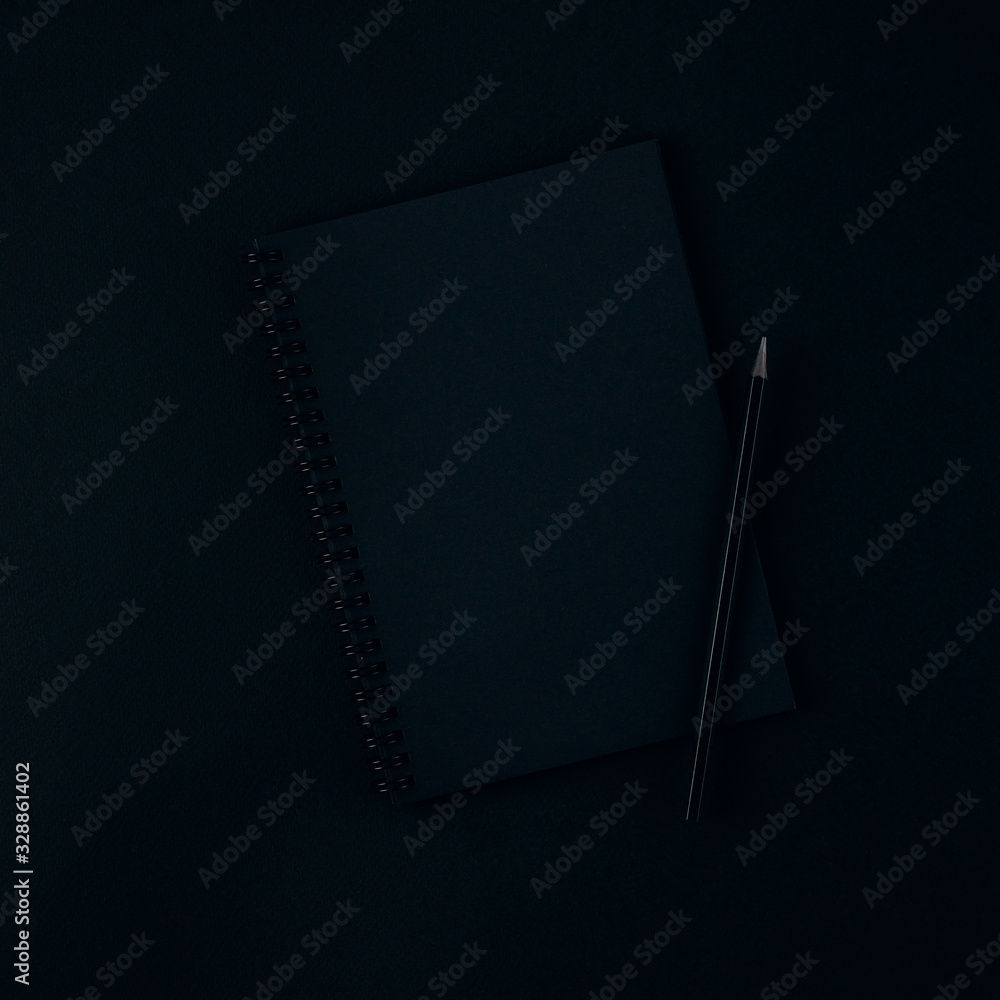 A black notebook and pencil on a dark black background A black notebook and pencil on a dark black background