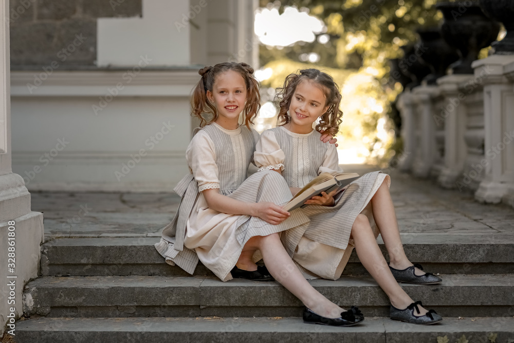 Two girls of primary school schoolgirls read a book in the courtyard of the academy.