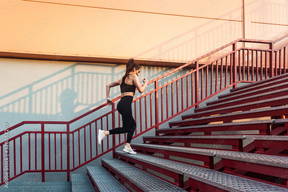 Motivated runner athlete, fit confident girl in black sportswear, tight pants and top, running up stairs doing cardio training, jogging workouts for weight loss. Health care, sport activity outdoor Motivated runner athlete, fit confident girl in black sportswear, tight pants and top, running up stairs doing cardio training, jogging workouts for weight loss. Health care, sport activity outdoor