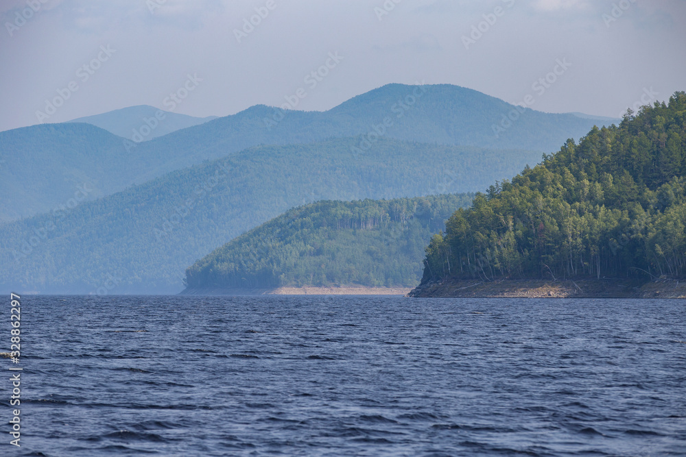 Beautiful landscape. Zeya reservoir, Amur region. A beautiful rocky shore with tall green trees goes into the calm blue waters of the reservoir. Beautiful landscape. Zeya reservoir, Amur region. A beautiful rocky shore with tall green trees goes into the calm blue waters of the reservoir.
